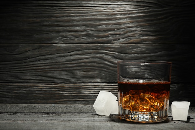 Vaso de whisky y cubitos de hielo sobre fondo de madera oscura, espacio para texto