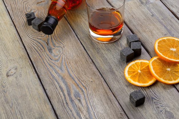 Vaso de whisky con fruta naranja cortada en madera oscura