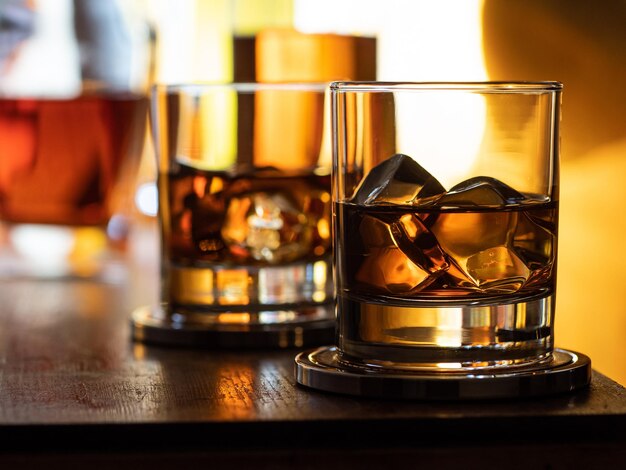 Vaso de whisky con hielo en una barra de madera