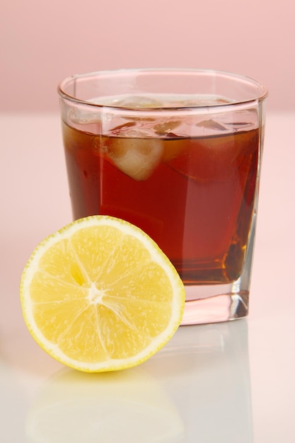 Vaso de whisky con hielo y limón sobre fondo rojo.