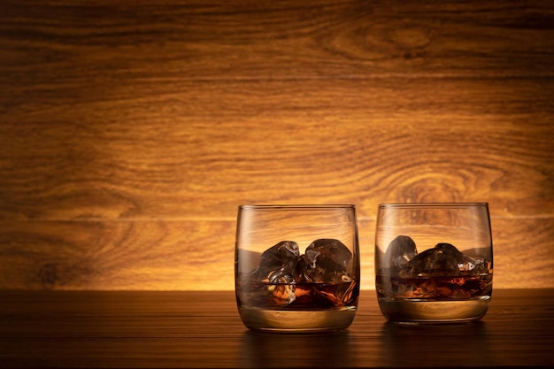 Vaso de whisky con hielo sobre un fondo de madera. Dos vasos de whisky en la mesa