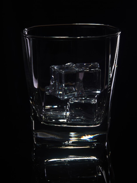 Vaso de whisky con hielo sobre un fondo negro con reflejo