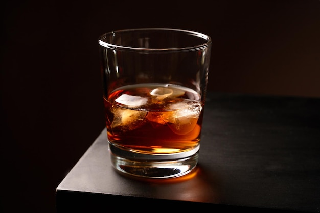Un vaso de whisky con hielo sobre una mesa de madera Clave baja