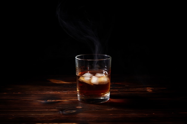 Vaso de whisky con humo y hielo en una mesa de madera