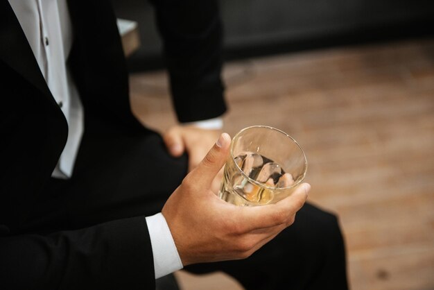 Un vaso de whisky en la mano de un hombre con traje negro.