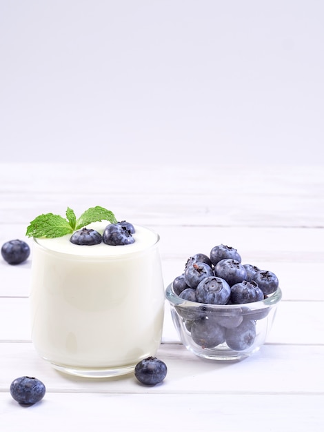 Vaso de yogur de arándanos en mesa de madera blanca