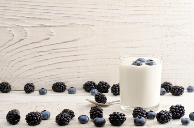 Vaso de yogur con bayas, arándanos, moras y arándanos en el borde, fondo claro