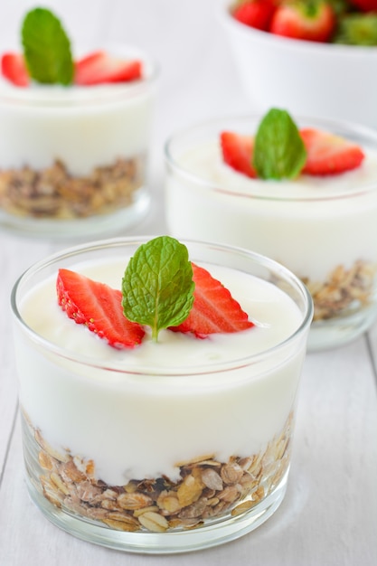 Vaso de yogur con cereales y fresas en mesa de madera blanca