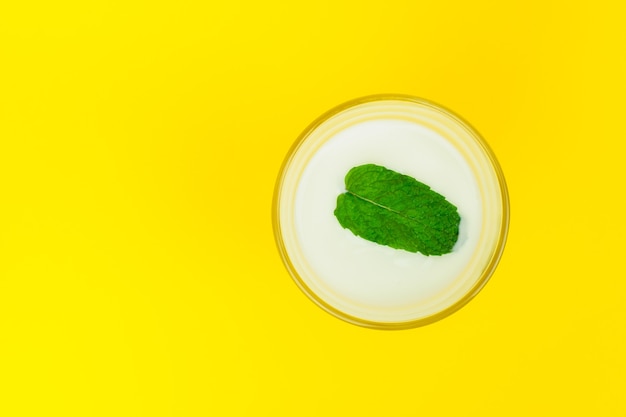 Foto un vaso con yogur natural y una hoja de menta. vista superior sobre fondo amarillo brillante