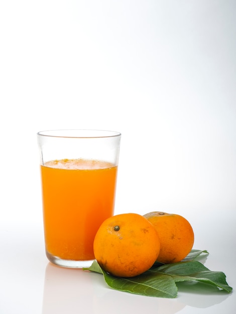 Vaso con zumo de naranja y frutas con hojas verdes.