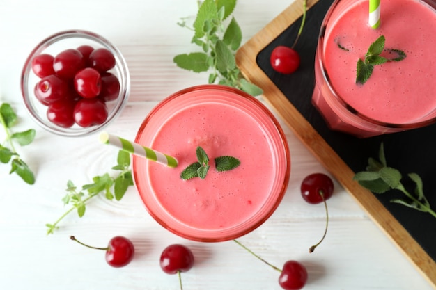 Vasos de batido de cerezas e ingredientes en la mesa de madera blanca