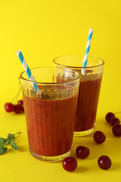 Vasos de batido de cerezas e ingredientes sobre fondo amarillo