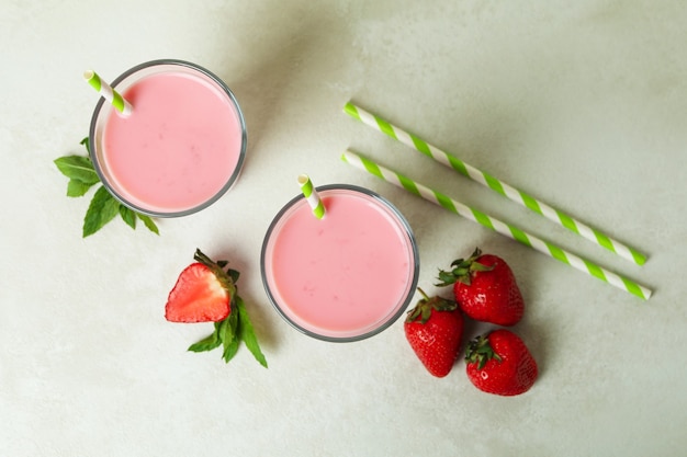 Vasos de batido de fresa e ingredientes en la mesa con textura blanca