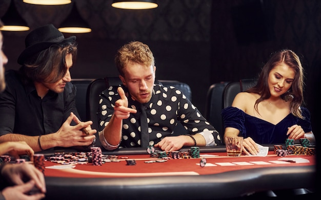 Con vasos de bebida. Grupo de jóvenes elegantes que juegan al póker en el casino juntos