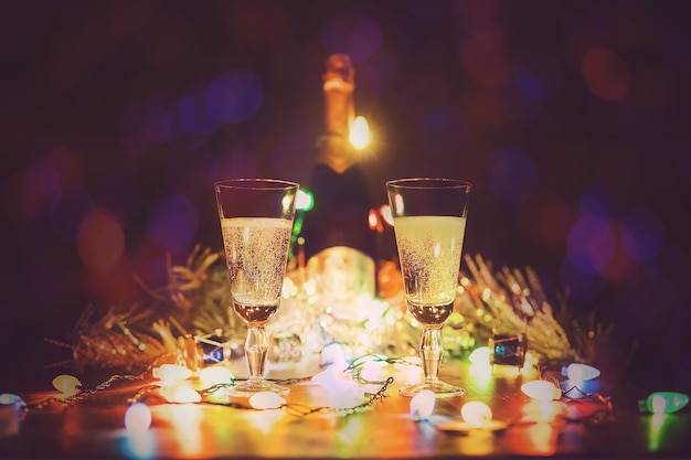 vasos con champán de pie sobre una mesa de madera con el telón de fondo de las luces de una guirnalda. Dos copas de champán brindando contra el fondo de luces bokeh