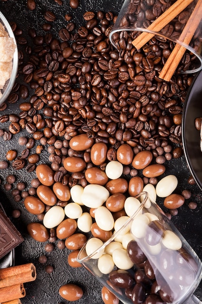 Vasos derramados con granos de café y cacahuetes en chocolate sobre un fondo de madera oscura en la foto de estudio junto a otros dulces