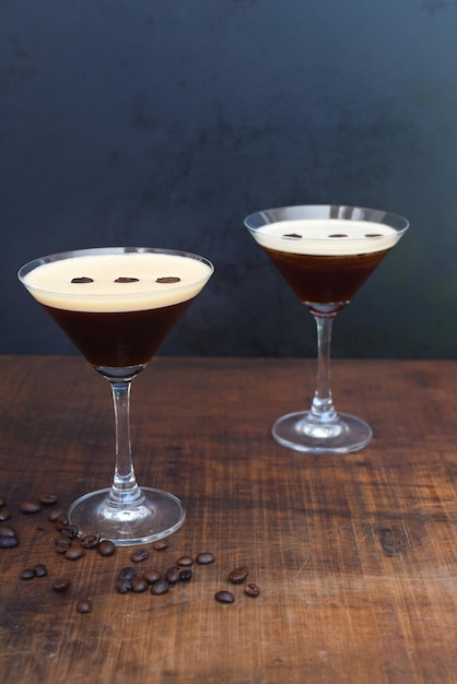 Vasos de espresso martini con granos de café sobre una mesa de madera y fondo negro