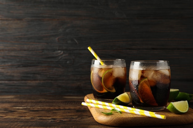 Vasos con hielo cola, rodajas de limón y túbulos sobre fondo de madera