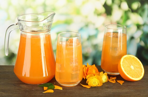 Vasos y jarra de jugo de naranja sobre mesa de madera sobre fondo verde