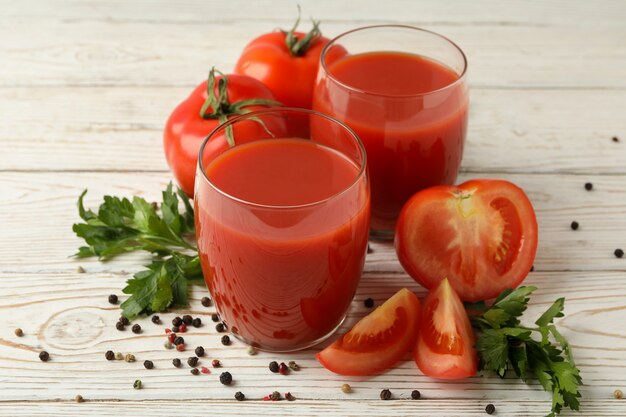 Vasos con jugo de tomate, tomates y especias en madera