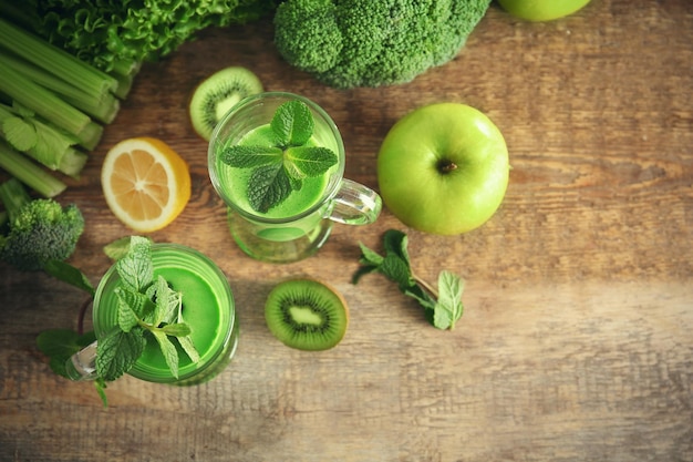 Vasos de jugo verde saludable con verduras y frutas en la mesa de madera