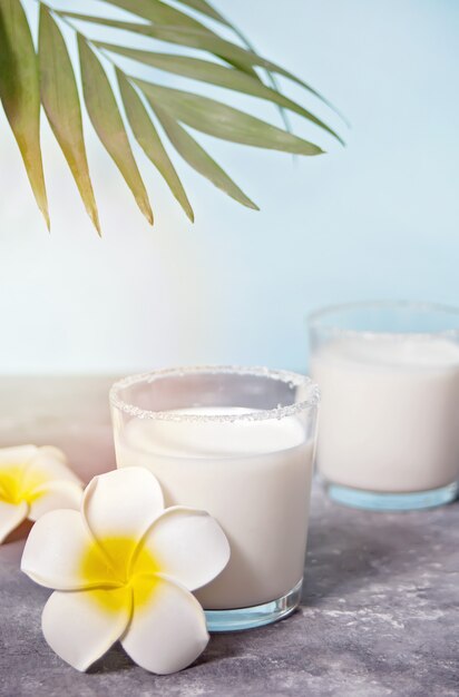 Vasos de leche de coco con flor de plumeria y hoja de palma