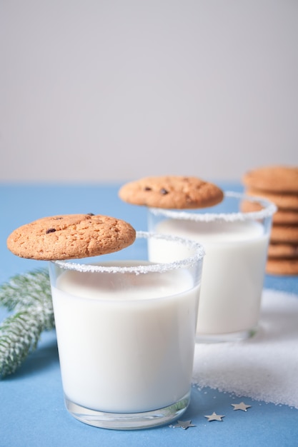 Vasos de leche, galletas, rama de árbol de navidad en azul