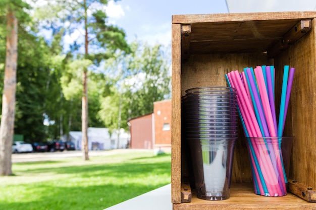 Vasos y pajitas de plástico desechables en una caja de madera Foto horizontal