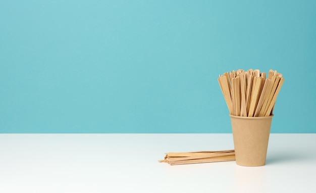 Vasos de papel desechables y palos de madera en el espacio de copia de fondo azul de mesa blanca