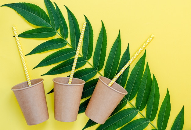 Vasos de papel ecológico con pajitas y hojas verdes sobre fondo amarillo. Estilo de vida libre de plástico