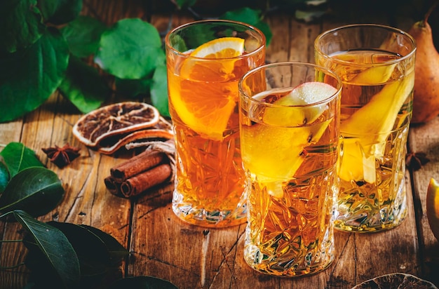 Vasos de sidra manzana pera y bebidas de naranja Cóctel de frutas fermentadas con bajo contenido de alcohol sobre fondo de mesa de madera vieja con hojas