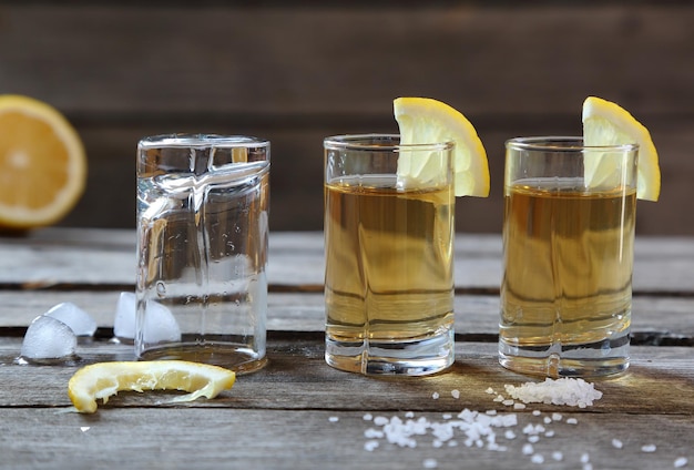 Vasos de tequila con limón y sal en una mesa de madera