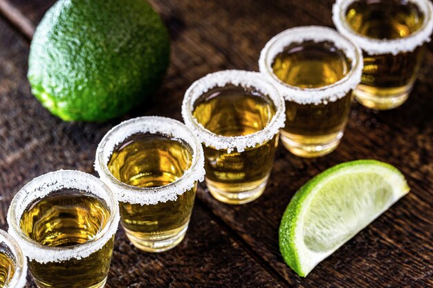 Vasos de tequila mexicano de oro con limón y sal sobre superficie de madera