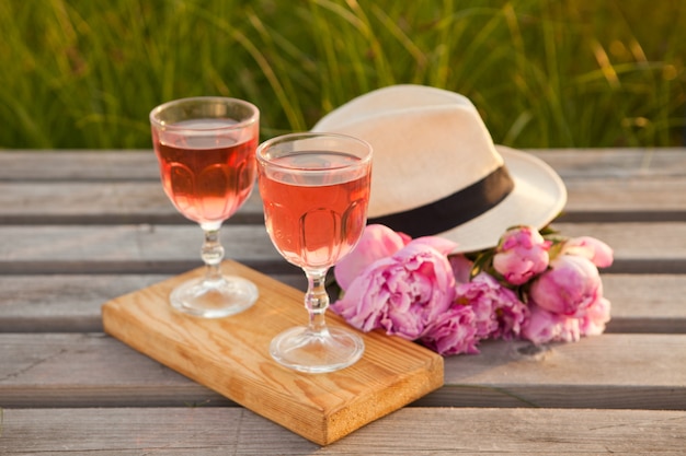 Vasos con vino rosado y ramo de peonía rosa deliciosa bebida refrescante flor floreciente y sombrero