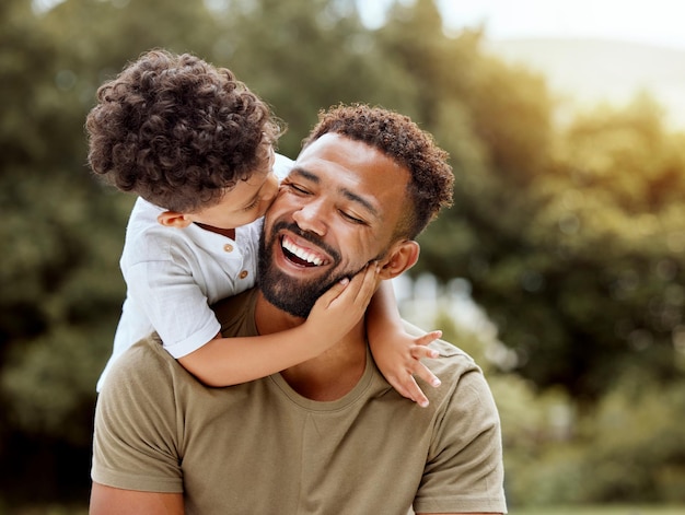 Vater Bindungskuss und Junge Kind Umarmung glücklich in der Natur mit guter Zeit zusammen im Freien Glück lachend und Familienliebe eines Vaters und eines Kindes in einem Park, der die Natur genießt und sich mit Sorgfalt und einem Lächeln umarmt