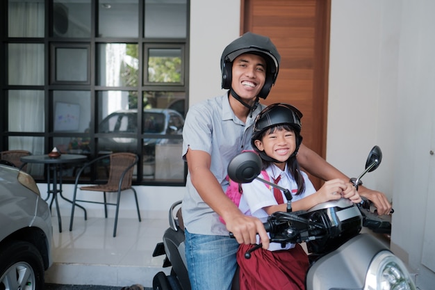 Vater bringt seine Tochter morgens mit dem Motorrad zur Schule. asiatischer Grundschüler in Uniform, der zurück zur Schule geht