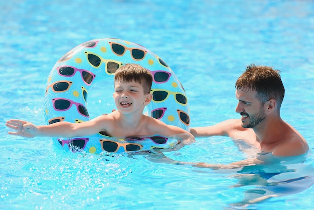 Vater bringt seinem kleinen Sohn bei, im Schwimmbad mit aufblasbarem Ring zu schwimmen