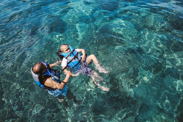 Vater bringt seinem Sohn bei, auf dem Meer zu schwimmen und aus Sicherheitsgründen eine Schwimmweste zu tragen