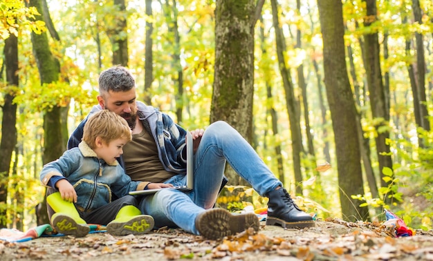 Vater bringt seinem Sohn bei, moderne Technologie zu verwenden. Vereint mit der Natur. Ökologie-Lektion. Waldschule und Ökologieunterricht. Mann bärtiger Vater und kleiner Sohn mit Laptop im Wald. Ökologische Erziehung