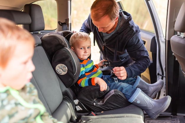 Vater, der den Sicherheitsgurt für seinen kleinen Jungen in seinem Autositz anschnallt.