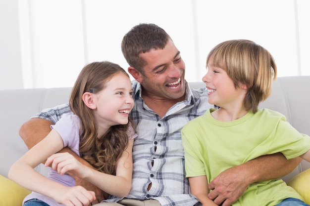 Vater, der Sohn und Tochter beim Sitzen auf Sofa kitzelt