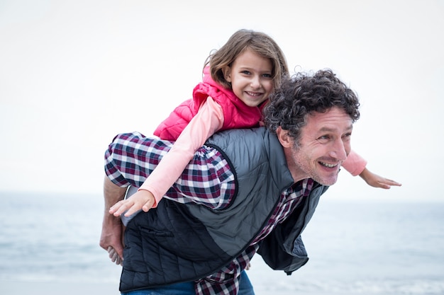 Vater, der Tochter am Strand huckepack trägt