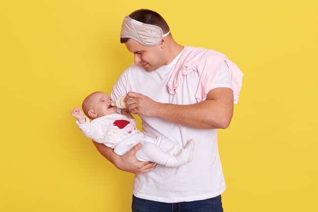 Vater füttert kleine Tochter mit Babynahrung von Flasche, während lokalisiert über gelber Wand steht