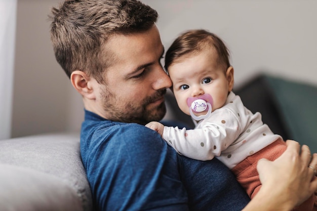 Vater hält Babymädchen in den Armen, während er auf dem Sofa sitzt