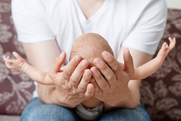 Vater hält den Kopf seines neugeborenen Sohnes in Händen. Das Baby auf Händen bei Papa.