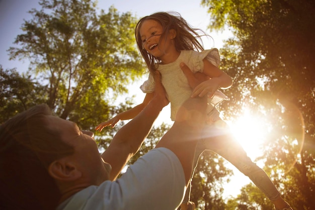 Vater hält kleine Tochter an den Händen im Park hoch