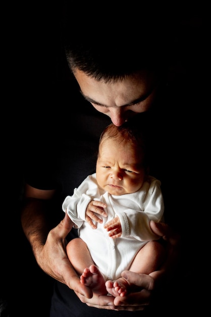 Vater hält seinen 15 Tage alten Sohn in der Hand auf schwarzem Hintergrund. Baby liegt auf seinem Vater.