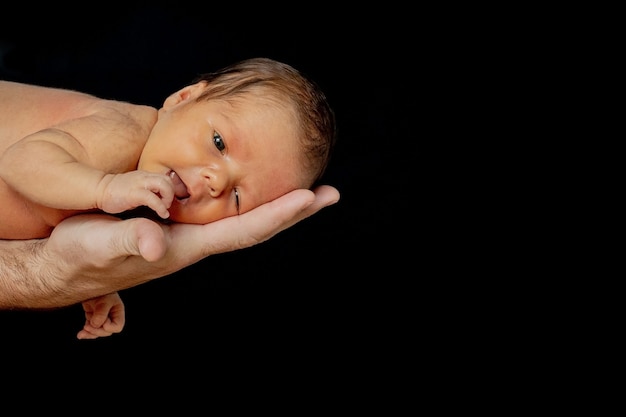 Vater hält seinen 15 Tage alten Sohn in der Hand auf schwarzem Hintergrund.