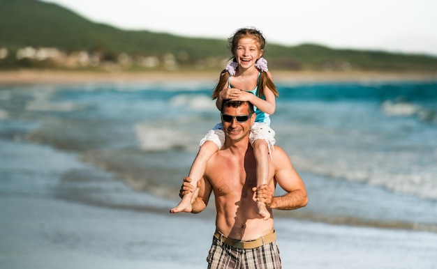 Vater hält Tochter im Rücken an der Küste und hat Spaß Familienvater und kleines hübsches Kind am Strand im Sommer