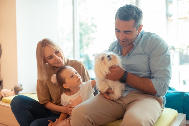 Vater hält weißen, flauschigen Hund, der neben Frau und Tochter sitzt